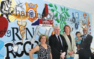 A wall mural depicting the various curriculums offered at Roanoke-Chowan Community College was unveiled at the college’s Student Center on the first day of classes Aug. 18.  The mural was painted by Marvin Ryan, a student in the college’s Fine Arts Department, and artist Jim Messer.  Shown are: (from left) Amy Braswell, Executive Director of the Ahoskie Chamber of Commerce; Marvin Jones, Executive Director of the Chowan Discovery Group; Jim Messer, Chairman of the RCCC Fine Arts Department; and RCCC President Dr. Michael Elam (shown with grandson, Gabriel. Staff Photo by Gene Motley