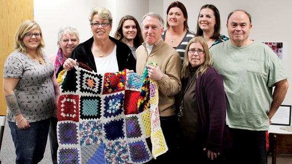 Scott Mason (front center; aka The Tarheel Traveler) joins with Rita New in holding a colorful lapghan created by the “Granny Squares of Love.” Others shown, from left, on the front row are Jen Meyers and Betty Jones; along with, back row from left, Glema Demario, Merindy Piland, Cassandra Daughtry, Kendra Evans, and Danny Bowman. Photo by Macaulay Chilaka Jr.