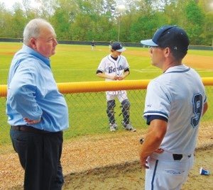 As a player in the background wears one of the uniforms during pre-game warm-ups, Ronald D. Cooke (left) chats in the dugout with current Falcons baseball coach Bobby Harmon (right). The late coach’s initials, ‘REC’, are visible on the sleeves of the new uniforms. Photo by JW “Russ” Russell