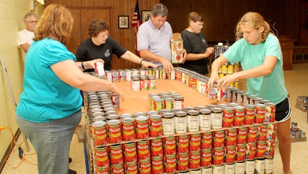 From left, Ahoskie United Methodist Church members Sally Barnes, Pat Bland, Richard Jernigan, Rodney Bland, and Cameron Basnight work as a team to position the cans of food that would later take the shape of a farm barn (as shown below, complete with an adjacent farm silo). Also shown in the photo is Jim White (leaning against the wall) who assisted with cutting sheets of wood used to stack the cans by the different levels of the barn. Staff Photos by Cal Bryant