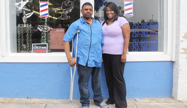Rhynda Riddick stands with his friend, Natesha Giddings, in front of “The Barbershop” in Ahoskie. Despite losing a leg in a motor vehicle accident in 1993, Riddick puts in long hours daily, mostly standing up, as a barber….a job that’s tough on his prosthetic leg. Staff Photo by Cameron Jernigan